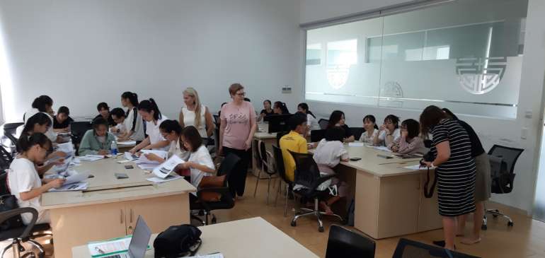 Intensive course taking place in Vitnam. Students sit and work at the tables and teachers help them out.