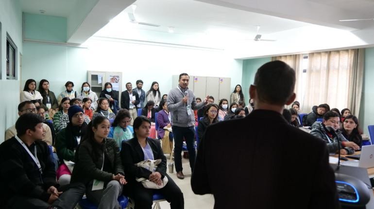 people sitting in a classroom and listening to a speaker, who is standing in the middle of the room